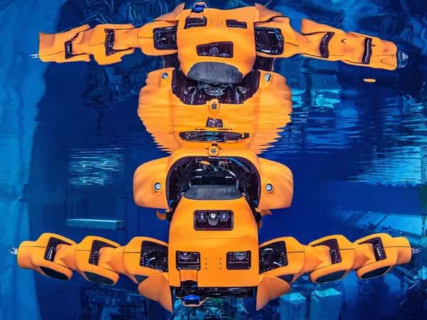 Aquanaut — оранжевый полугуманоид в воде с вытянутыми руками и его зеркальным отражением на поверхности.