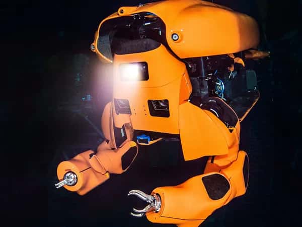 Aquanaut — оранжевый полугуманоидный робот-субмарина с захватными руками светит фонарём под водой.
