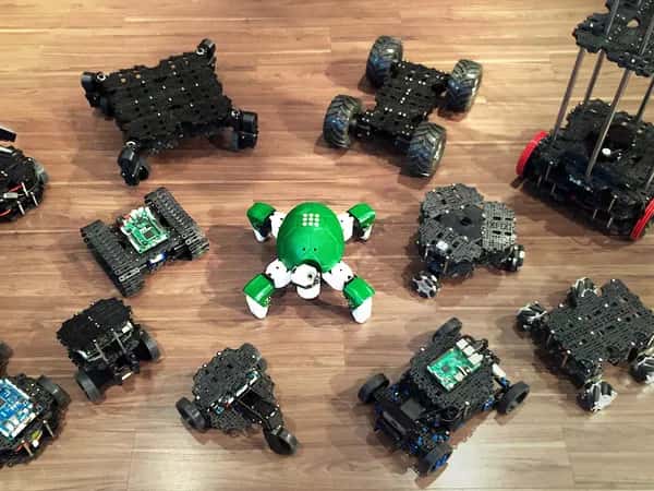 Дюжина вариантов TurtleBot 3 разных форм и размеров на деревянном полу.