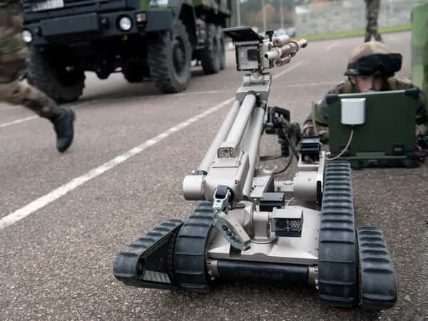 Военный лежит на улице перед ноутбуком. Перед ним — PackBot, сбоку — танк.