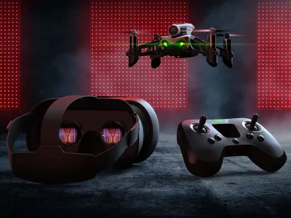 Mambo FPV — белый дрон со светящимися зелёными глазами в полёте на заднем плане, на переднем — пульт управления и VR-очки.