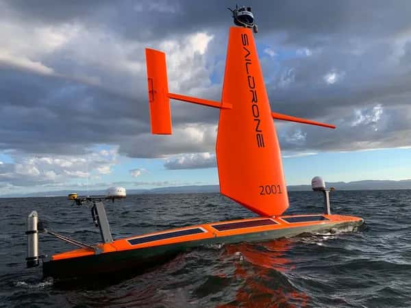 Saildrone — беспилотное надводное судно. Имеет горизонтальный оранжевый корпус с несколькими солнечными панелями, высокий вертикальный оранжевый парус и руль, расположенный параллельно поверхности моря.