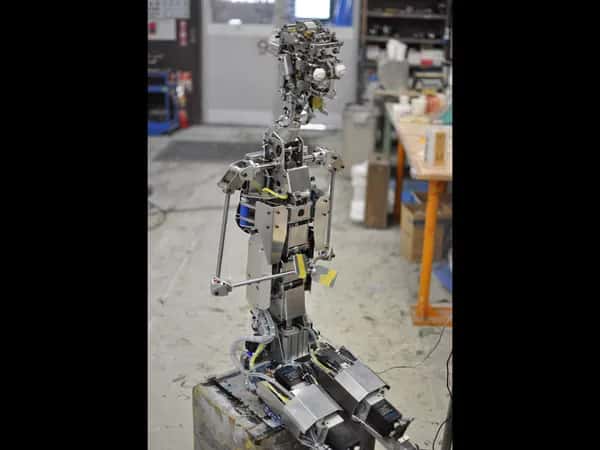Geminoid F — вид в полный рост на металлический и электронный скелет сидящего робота.