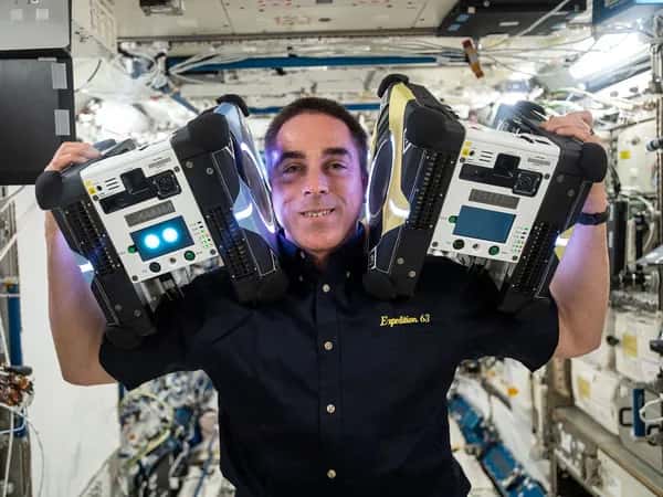 Astrobee — улыбающийся астронавт на космической станции держит на каждом плече по квадратному роботу — оба крупнее его головы.