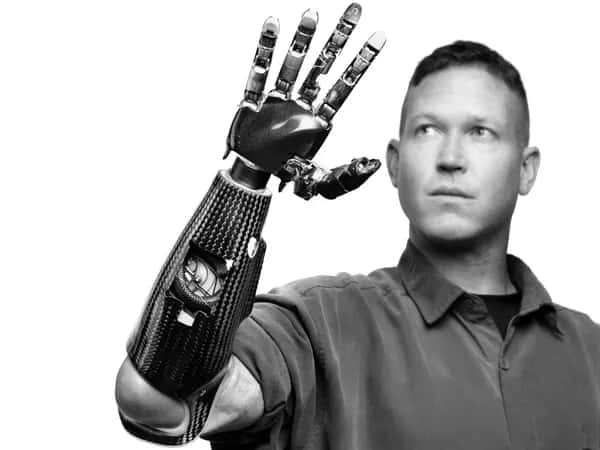 Modular Prosthetic Limb — чёрно-белая современная фотография: мужчина смотрит на свою роботизированную руку, поднятую перед лицом.