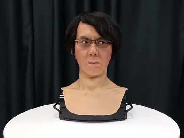 Geminoid HI — голова робота — в очках, с копной чёрных волос и выразительным лицом — стоит на столе.