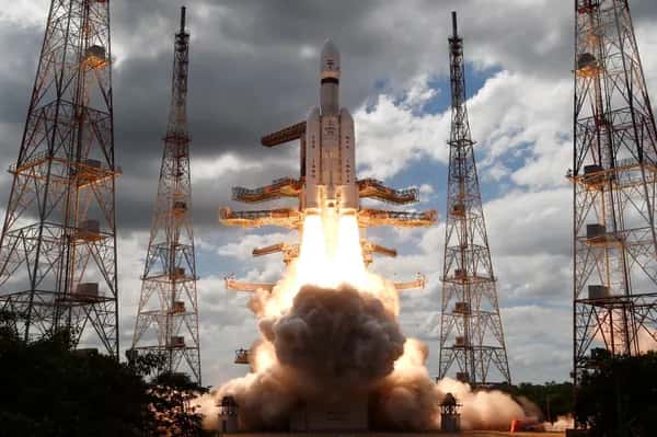 Pragyan — запуск космического аппарата Chandrayaan-3: яркая жёлтая вспышка двигателей уносит его в частично облачное небо среди металлических антенных башен.
