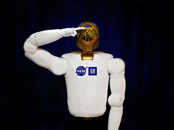 Robonaut 2 — торс робота-астронавта с золотым шлемом вместо головы и мягким белым корпусом. Одна рука поднята к голове в приветственном салюте.