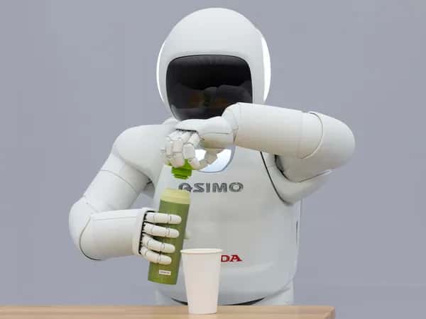 ASIMO от Honda открывает бутылку с зелёной жидкостью перед стаканом.