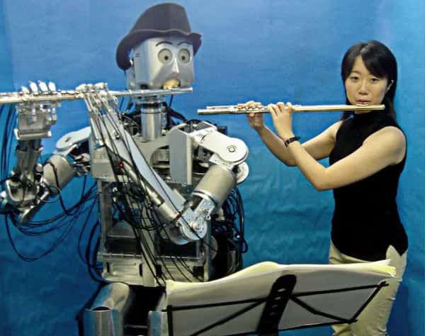 Waseda Flutist — человекоразмерный гуманоидный робот и женщина сидят рядом и играют на флейте, глядя на ноты на пюпитре.