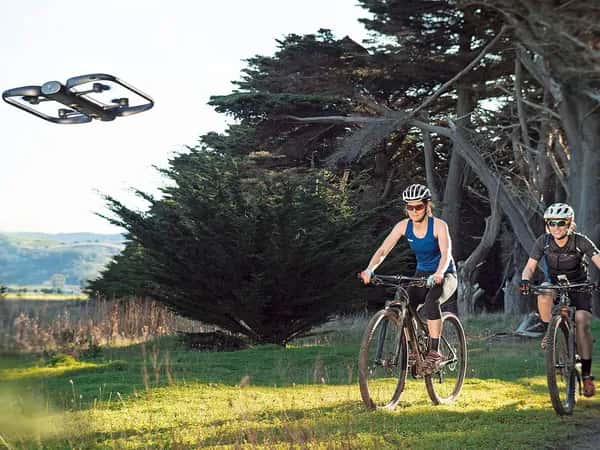 Skydio R1 — двое в шлемах едут на велосипеде по живописной местности, перед ними летит чёрный дрон.