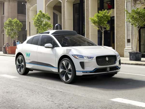 Waymo — белый компактный автомобиль с небольшим чёрным куполом на крыше на городской дороге.