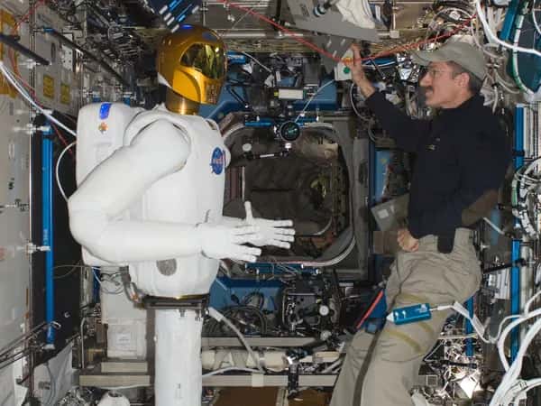Robonaut 2 — robonaut и астронавт в обычной одежде находятся внутри космической станции, заполненной оборудованием.