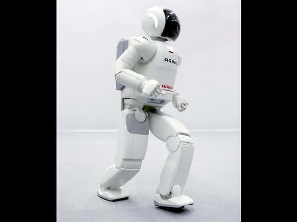 Двуногий белый робот ASIMO делает шаг.