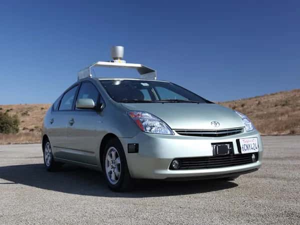 Google Self-Driving Car — автомобиль с камерами, радаром и багажником на крыше, несущим крупный лидар, стоит на дороге.
