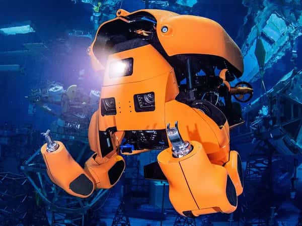 Aquanaut — оранжевый полугуманоидный робот-субмарина с захватными руками светит фонарём под водой.