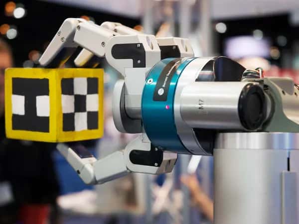 ARM — роботизированный захват удерживает пальцами жёлтый кубик с чёрно-белым узором.