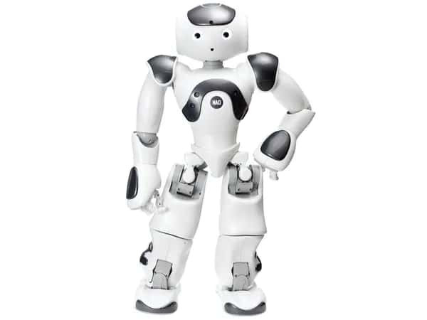 Nao — дружелюбный мультяшный гуманоидный робот бело-серебристого цвета — стоит, подбоченившись. У него два глаза и небольшое отверстие, образующее рот.