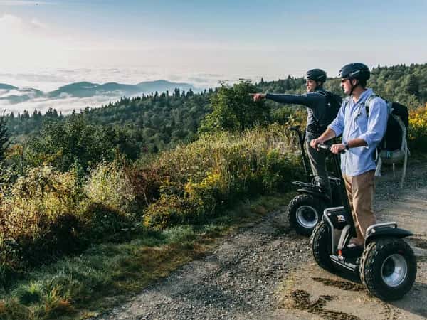 Двое на Segway с широкими внедорожными колёсами смотрят на живописный пейзаж.