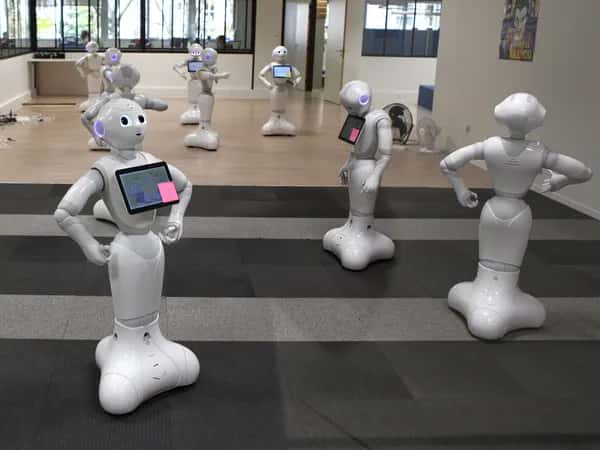 Девять роботов Pepper расставлены в большом зале в разных позах.