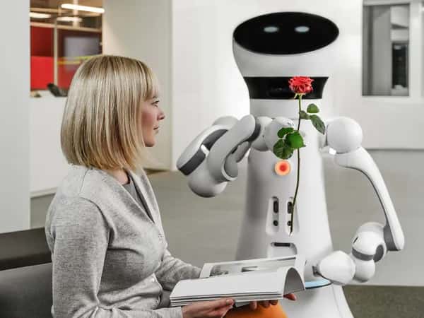 Care-O-bot 4 — робот протягивает цветок сидящей женщине.