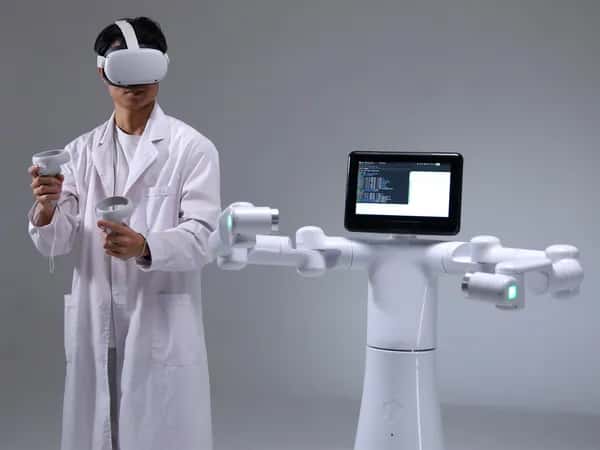 Mercury X1 — человек в лабораторном халате и VR-шлеме стоит рядом с колёсным роботом-гуманоидом, у которого вместо головы — планшет.