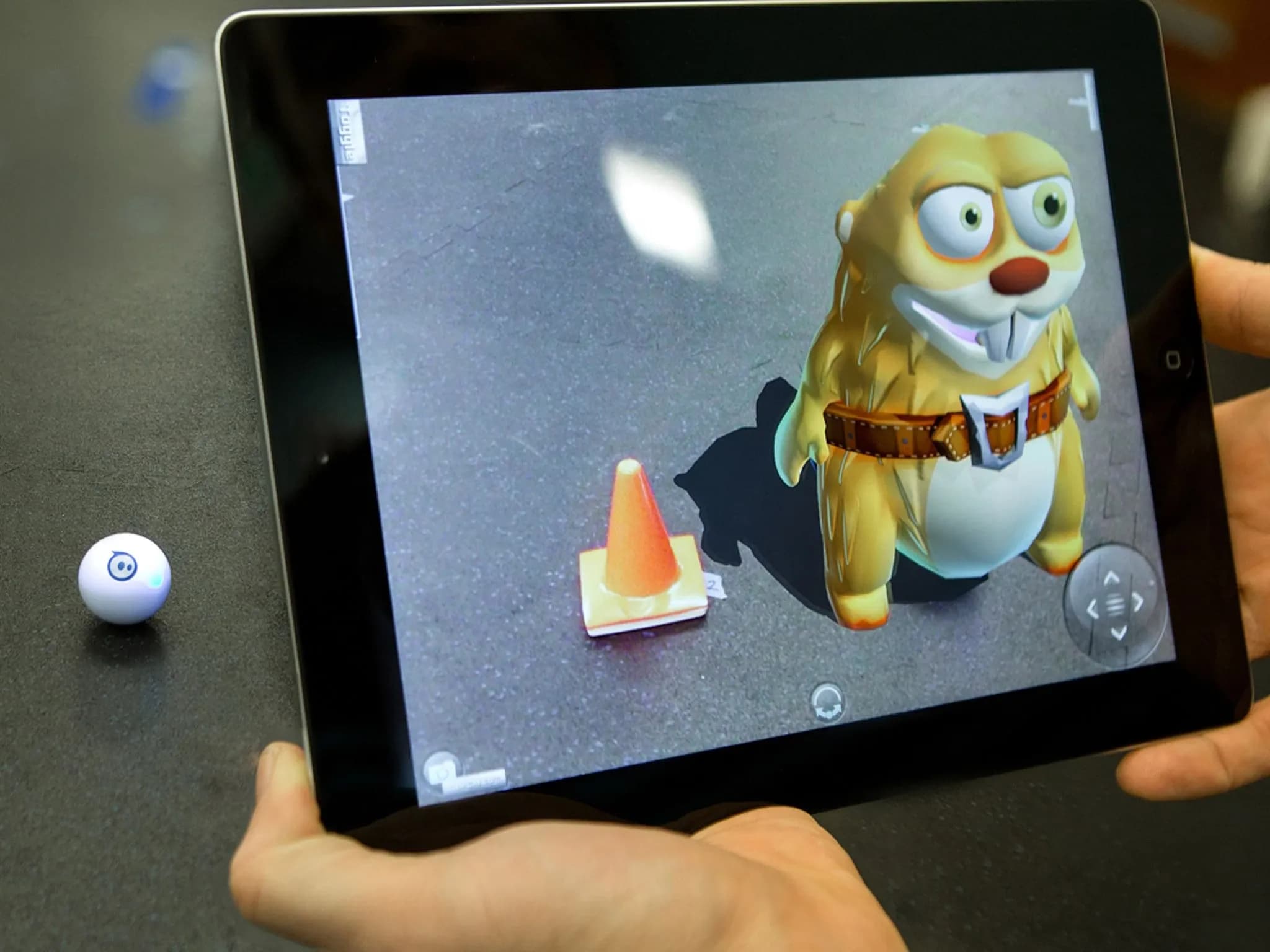 В руках держат iPad, на экране которого изображён мультяшный жёлтый бобёр рядом с оранжевым дорожным конусом.