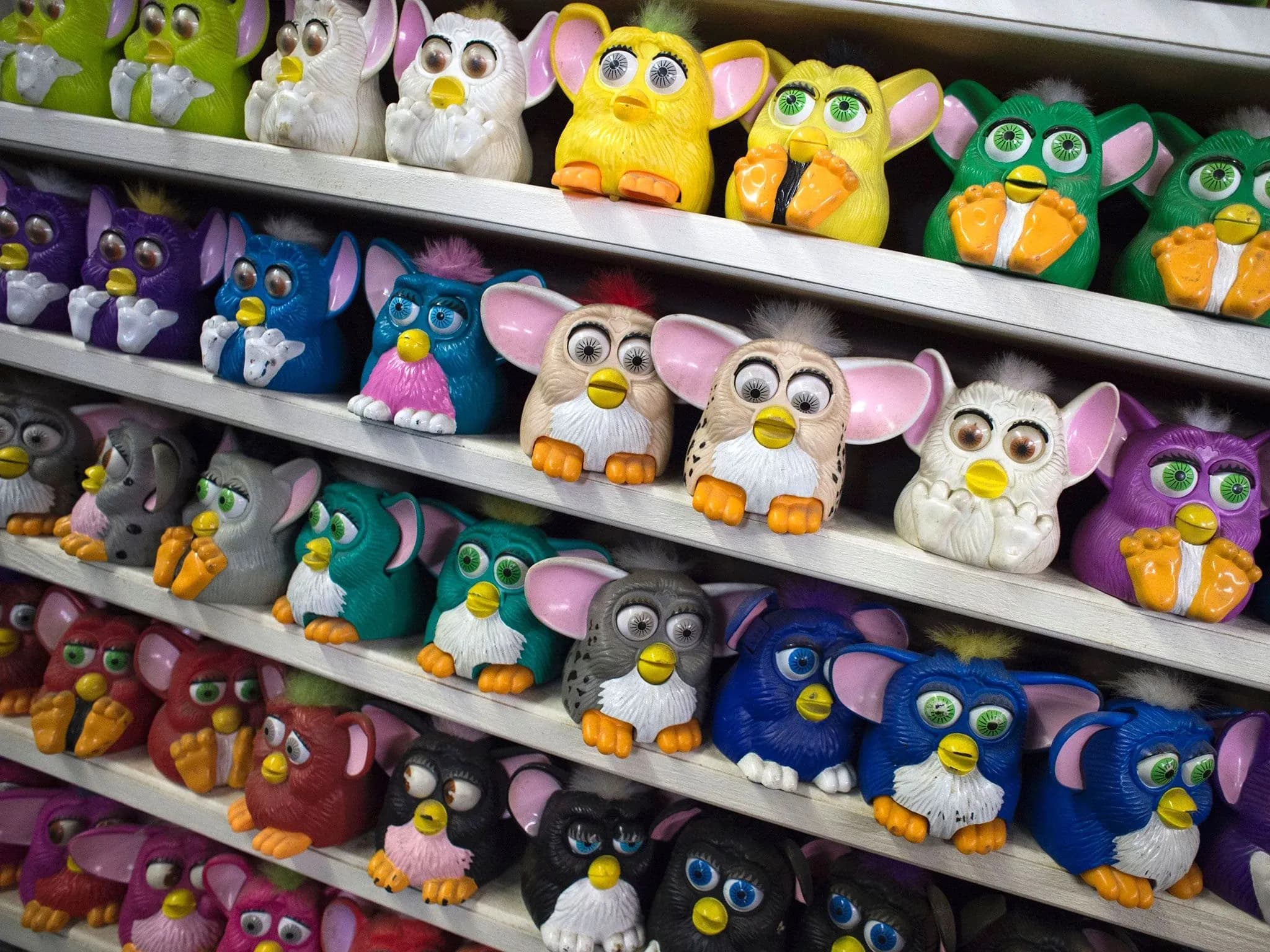 Почти 40 разноцветных роботов Furby расставлены на 5 полках.