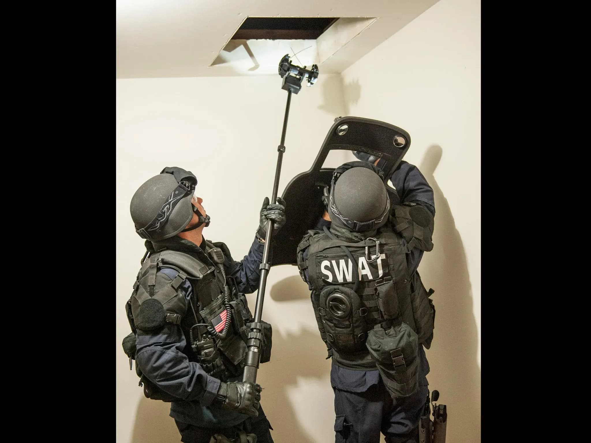 Двое бойцов SWAT удерживают шест с Throwbot на конце, поднося его к отверстию в крыше.