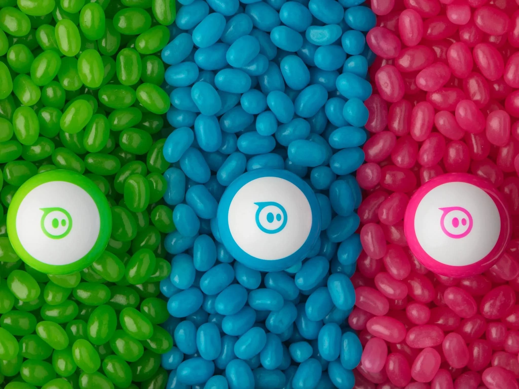 Три кучки разноцветных мармеладных конфет с цветами, совпадающими с Sphero mini сверху: зелёный, синий и розовый.