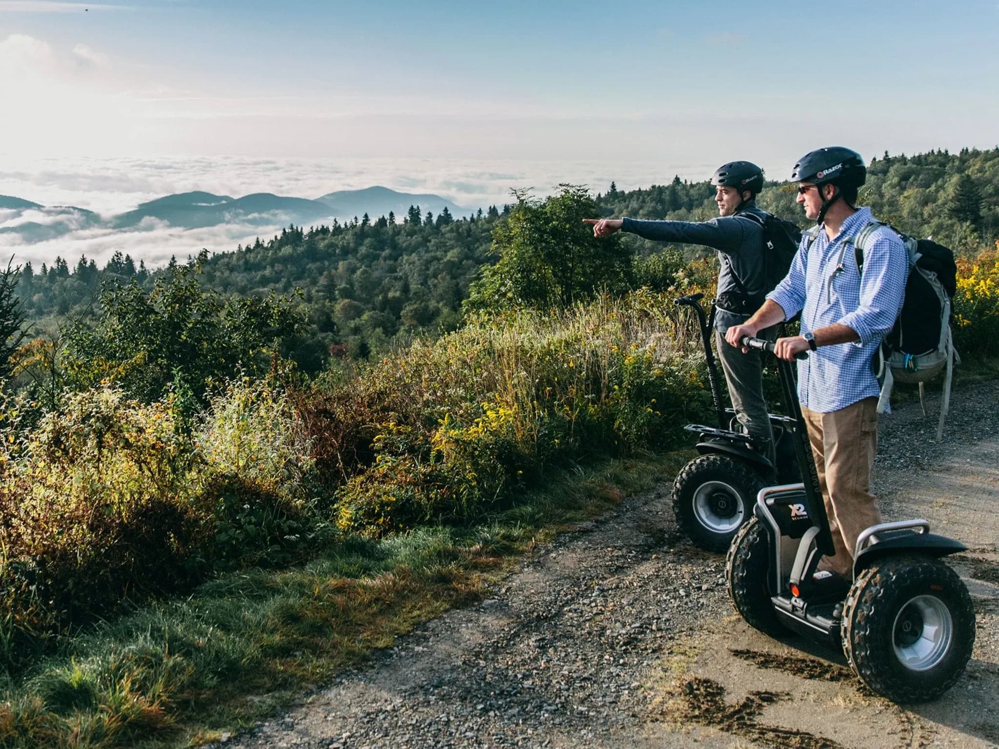 Двое на Segway с широкими внедорожными колёсами смотрят на живописный пейзаж.