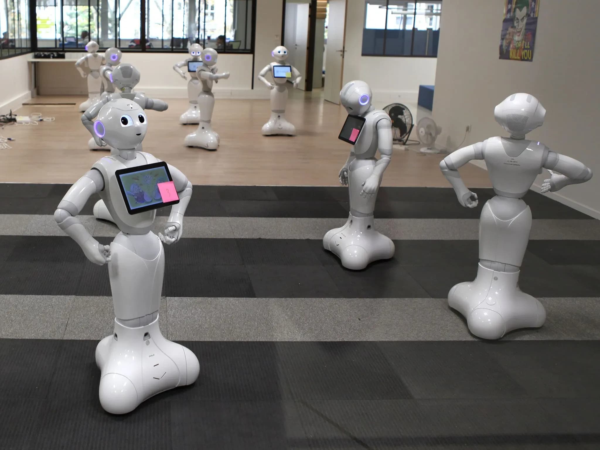 Девять роботов Pepper расставлены в большом зале в разных позах.