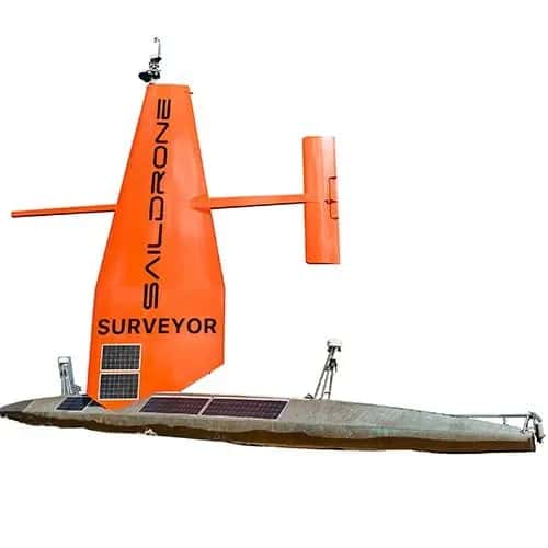 Saildrone — беспилотное надводное судно: горизонтальный серебристый корпус с несколькими солнечными панелями, высокий оранжевый парус с вертикальными солнечными панелями и параллельный руль.